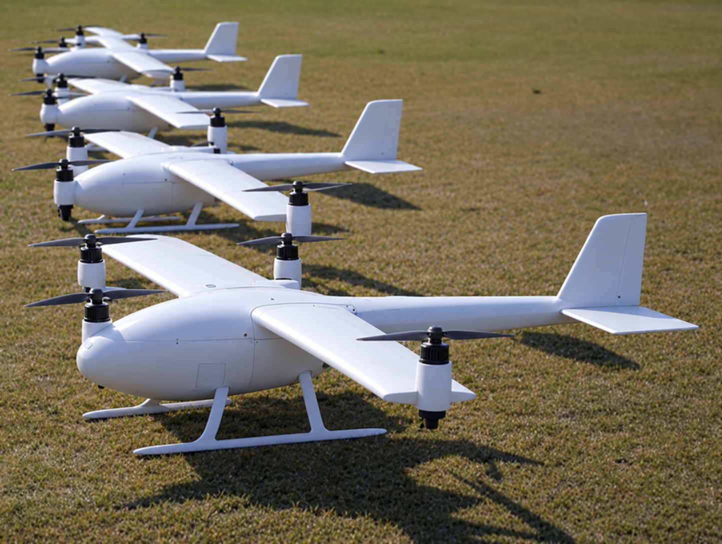 Fleet of white fixed-wing VTOL unmanned aircraft on grass